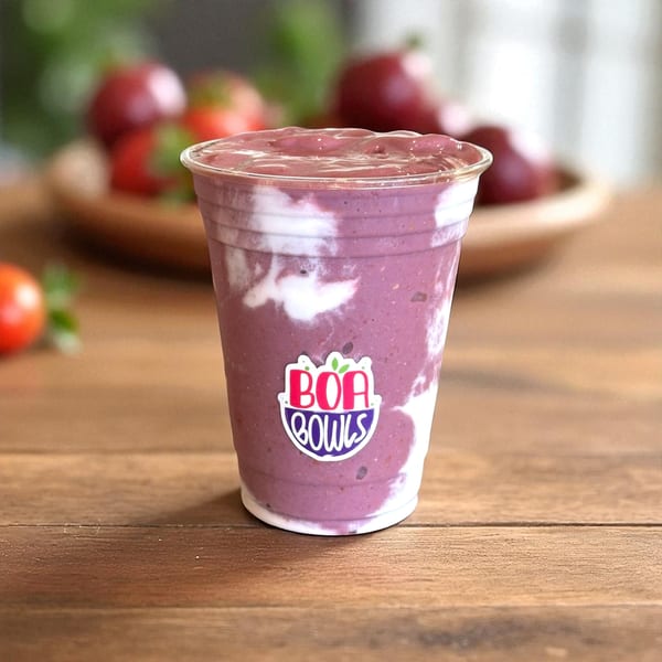 A Boa Bowls acai smoothie with white yogurt swirls in a clear cup on a wooden table.
