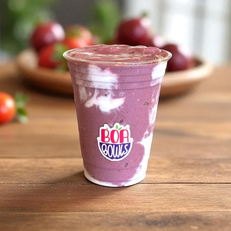 A Boa Bowls acai smoothie with white yogurt swirls in a clear cup on a wooden table.