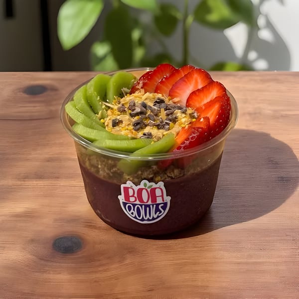 A Boa Bowls acai bowl with kiwi, strawberries, granola, and chocolate chips on a wooden table.