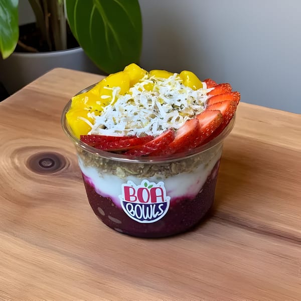 A Boa Bowls acai bowl with mango, strawberries, and shredded coconut on a wooden surface.