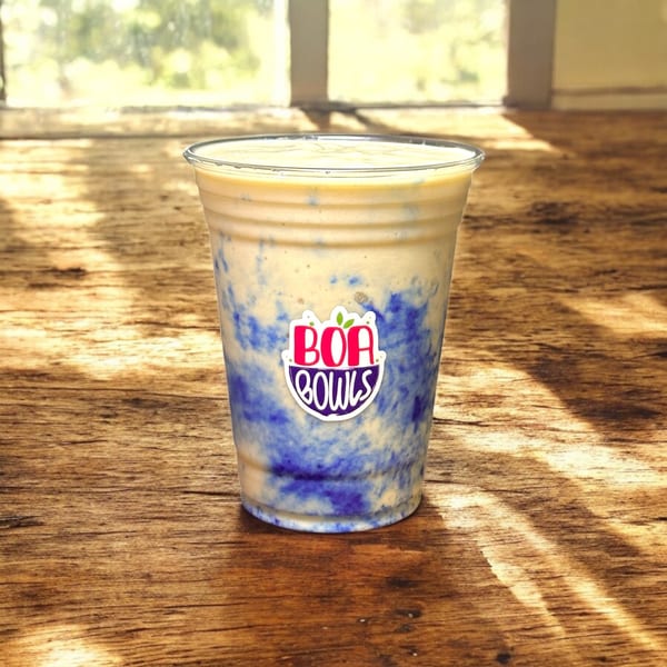 Boa Bowls acai smoothie with purple swirls, on a wooden table with a bright window background.