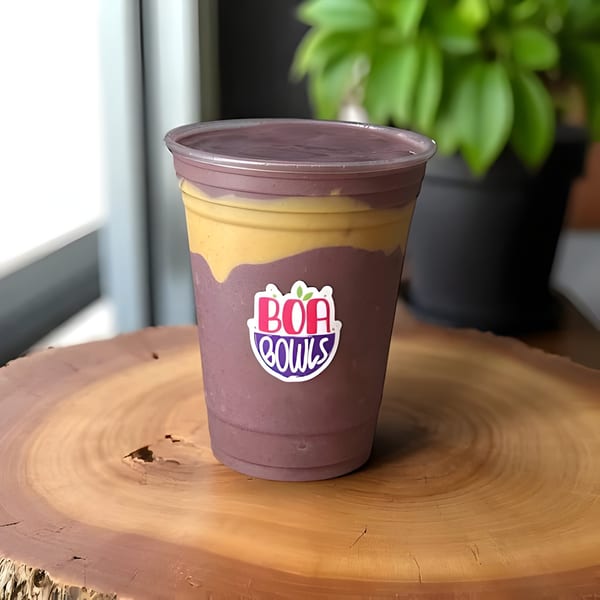 A Boa Bowls acai smoothie with purple and yellow layers sits on a wooden table.