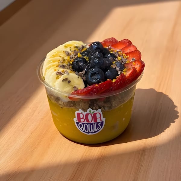 Boa Bowls acai bowl with bananas, blueberries, strawberries, and granola on a wooden surface.